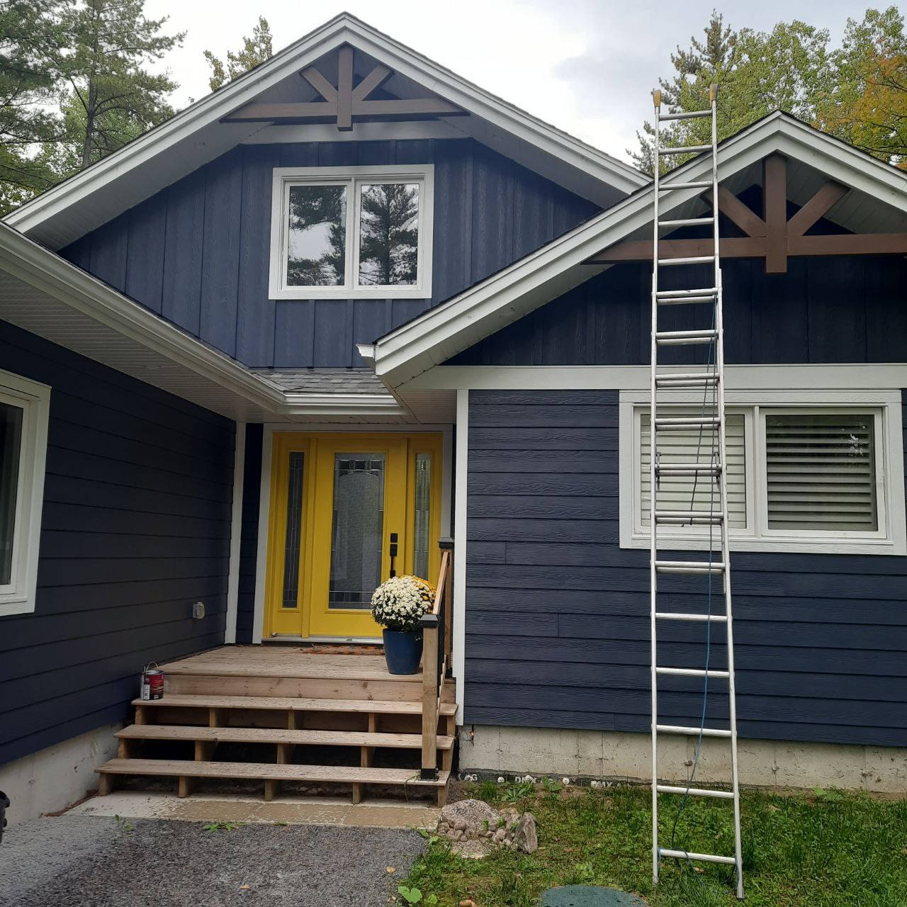 Freshly painted navy blue house with white trim and a yellow front door, ladder resting against the gable during an exterior repaint in Ottawa.
