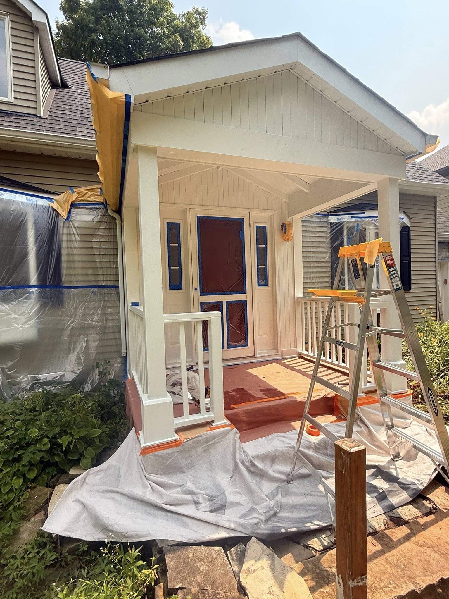 Front porch mid-repaint with drop sheets over the garden and freshly coated cream siding and columns