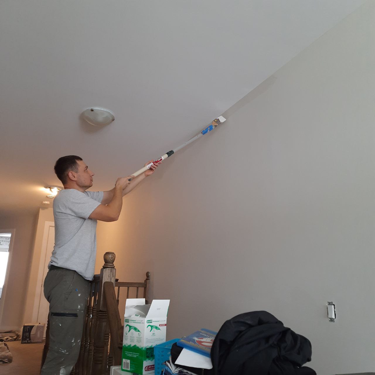 Painter rolling a ceiling with an extension pole in a cleared and sheeted interior room