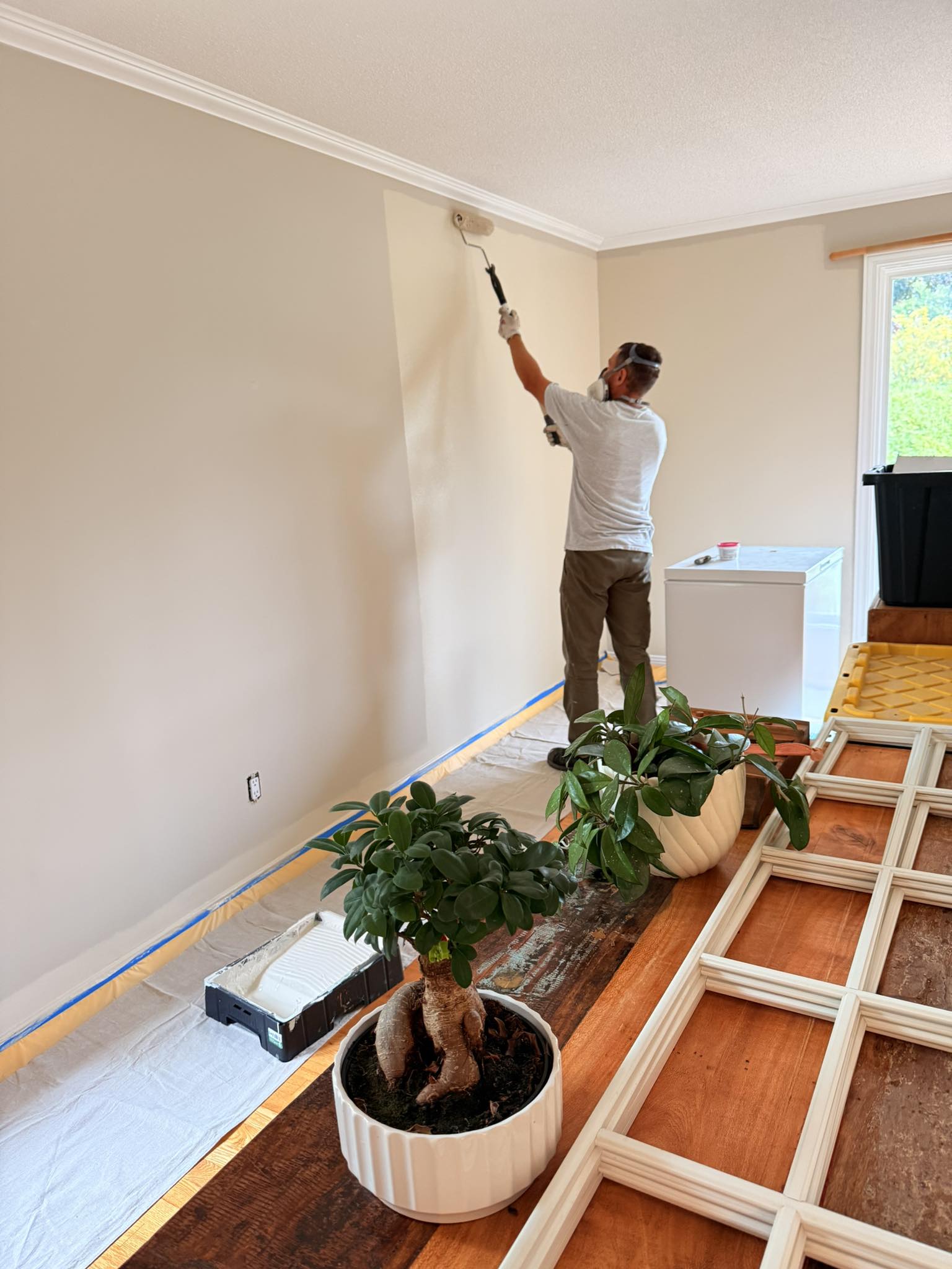 Interior repaint in progress — painter rolling a fresh coat with floors sheeted and trim removed